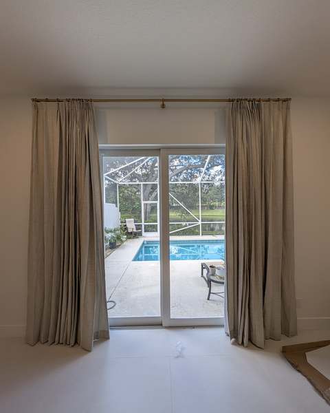 Curtain rod and floor-length linen curtains installed over sliding glass doors to a pool deck