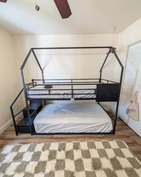 Black metal house-style loft bed with stairs and storage assembled in a child's bedroom