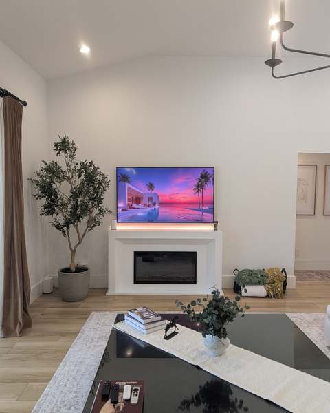 Flat-screen TV wall-mounted and leveled above a white fireplace console in a bright living room with vaulted ceilings